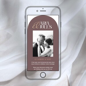 以下が含まれることがあります： スマートフォンには結婚式の招待状が表示されています。「ARIA JULES」という名前が金色の文字で書かれ、カップルの白黒写真と、結婚式の日付と場所を詳述するフランス語のテキストが含まれています。