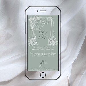 以下が含まれることがあります： スマートフォンには「ESRA & ADAM」の名前が書かれた結婚式の招待状が表示されています。デザインには花のモチーフとドレープが施され、フランス語で式典の詳細、日付、時間が記載されています。
