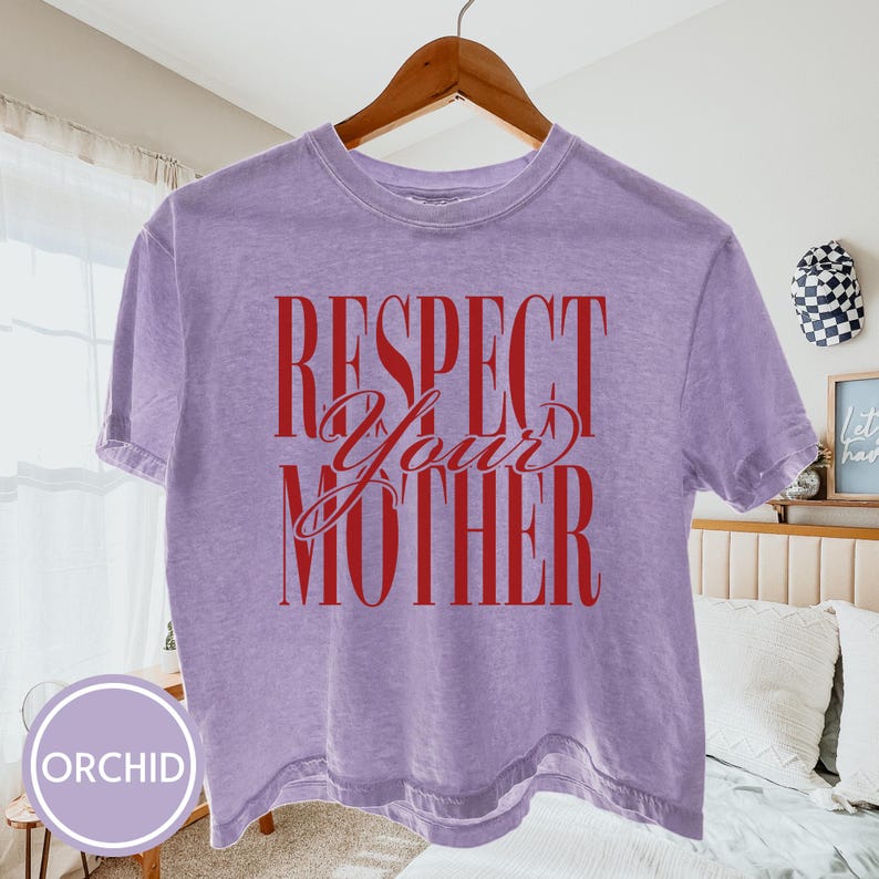 May include: A light purple short-sleeve t-shirt with a crew neckline. The shirt features the red text "RESPECT YOUR MOTHER" printed on the front in a combination of bold block lettering and a decorative script font for the word "Your".