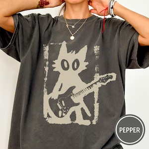 Puede incluir: Camiseta gris oscuro con un gato de dibujos animados beige tocando la guitarra. El gato est&aacute; dentro de un marco rectangular. La palabra "PEPPER" est&aacute; impresa en una etiqueta circular en la esquina inferior derecha.