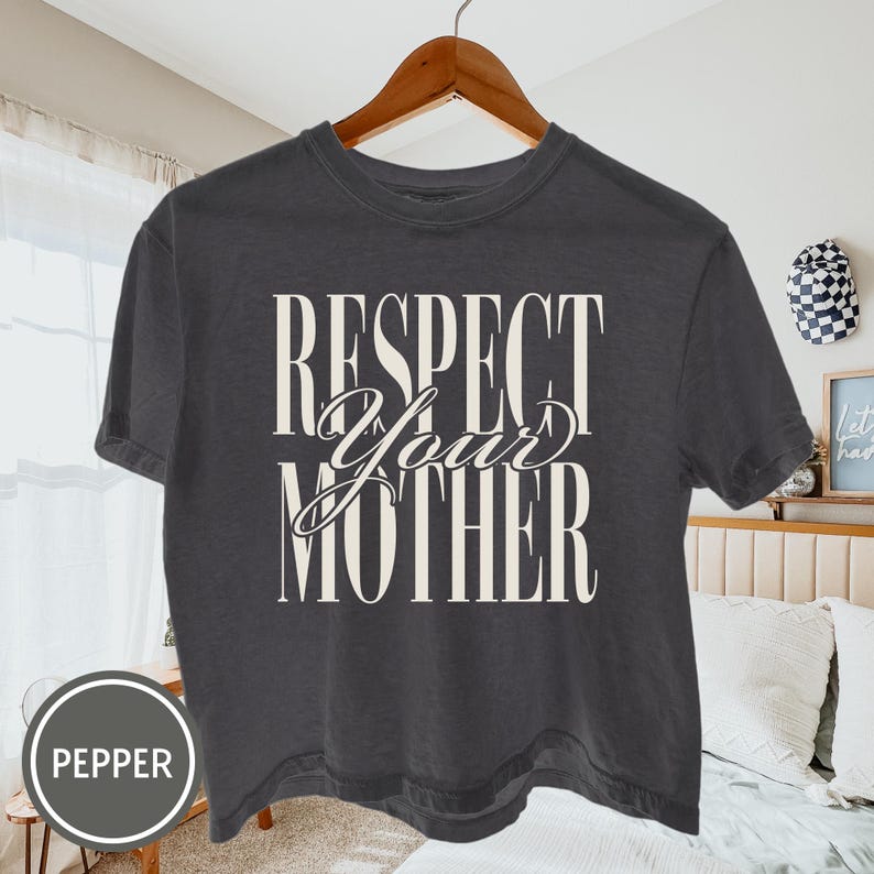 May include: A charcoal gray short-sleeve t-shirt featuring the white text "RESPECT YOUR MOTHER" printed on the front. The word "RESPECT" and "MOTHER" are in a tall, bold serif font, while "Your" is in a cursive script font.