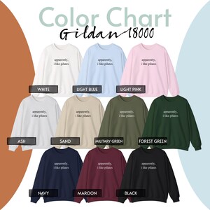 May include: A color chart showcasing Gildan 18000 sweatshirts in various colors, including white, light blue, and light pink. Each sweatshirt has the text "apparently, i like pilates" printed on the front. Other colors include ash, sand, military green, forest green, navy, maroon, and black.