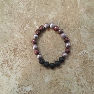 May include: A bracelet made of brown, purple, and black beads. The bracelet is made of lava rock and glass beads.