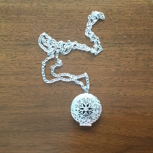 May include: A silver chain necklace with a round, silver pendant featuring a geometric design.