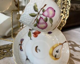 May include: White porcelain teacup and saucer set with a pear and insect design. The teacup features a handle and a pear branch illustration with pink and green accents. The saucer has a gold rim and a half-pear illustration.