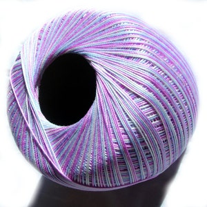 May include: A ball of multi-coloured yarn in shades of purple, blue, and white. The yarn is tightly wound, forming a circular shape with a dark hole in the centre. The yarn is likely used for knitting or crochet projects.