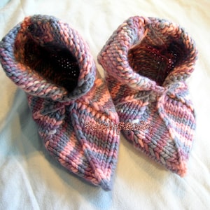May include: A pair of knitted pink and gray slipper socks with a folded cuff. The socks are made with a chunky yarn and have a soft, cozy look.