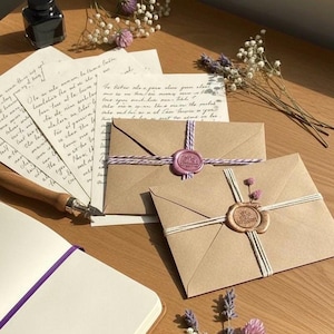 May include: A still-life composition featuring stationery items. Kraft paper envelopes are sealed with wax stamps and tied with twine. Handwritten letters, a calligraphy pen, ink bottle, and a notebook are also present, with floral accents.