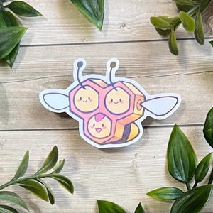 Könnte beinhalten: Ein gestanzter Aufkleber, der eine stilisierte, cartoonartige Kreatur zeigt, die aus drei miteinander verbundenen hexagonalen Waben in Rosa- und Gelbtönen besteht, mit zwei Antennen, zwei weißen Flügeln und drei lächelnden Gesichtern.