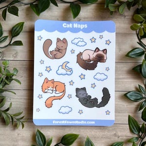 May include: A rectangular sticker sheet with a light blue border featuring the text Cat Naps at the top and forestfawnstudio.com at the bottom. The sheet contains illustrations of four sleeping cats in brown, cream, orange, and black, with clouds and stars.