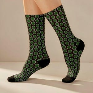 Puede incluir: Un par de calcetines con un patrón repetido de tréboles verdes delineados en blanco sobre un fondo marrón oscuro. Los calcetines tienen talones y dedos negros. Los calcetines son hasta la rodilla.