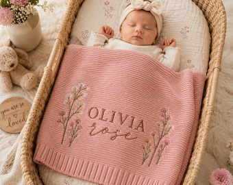 Peut inclure: Une couverture pour bébé en tricot rose poudré, ornée de tiges florales brodées de chaque côté et du nom OLIVIA rose cousu au centre. La couverture présente une bordure côtelée et recouvre un nourrisson endormi portant un bandeau crème.