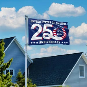 May include: A blue flag with white text that reads "UNITED STATES OF AMERICA 25TH ANNIVERSARY" with the years 1776-2026. The flag is waving in front of a blue sky and white clouds. The flag is on a flagpole in front of a house.