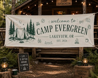 Peut inclure: Une bannière crème avec les mots "welcome to CAMP EVERGREEN" en vert, avec des illustrations d'arbres, d'une tente et d'icônes de camping. La bannière est suspendue devant un chalet en bois. Un petit tableau noir indique "LIFE IS BETTER AROUND THE CAMPFIRE."