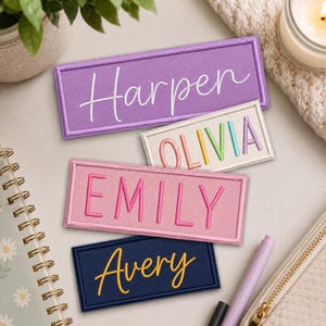 May include: Four rectangular embroidered patches with stitched borders. The top purple patch features the white script name Harper. The white patch displays the name OLIVIA in multicoloured block letters. The pink patch shows the name EMILY in pink block letters, and the bottom navy patch features the yellow script name Avery.