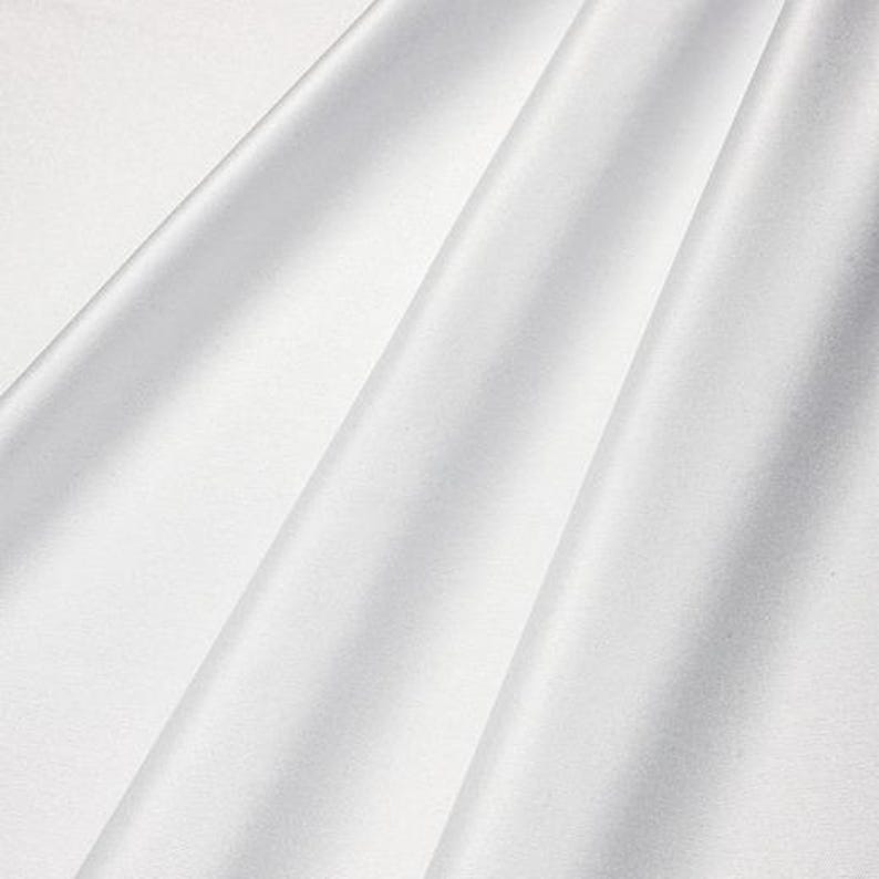 May include: A close-up of white fabric with soft folds and subtle shadows. The fabric appears smooth and has a slight sheen, suggesting a luxurious material. The folds create a sense of depth and texture.
