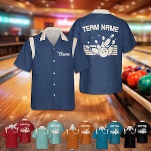 May include: Navy blue bowling shirt with white accents and a cream-colored collar. The front has a space for a name, and the back displays "TEAM NAME" above a bowling pin and ball graphic. Additional shirts in various colors are shown.
