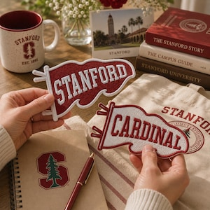 Puede incluir: Dos parches bordados en forma de banderín con el texto STANFORD en blanco sobre fondo rojo y CARDINAL en rojo sobre fondo blanco. Los parches se muestran sobre un fondo de artículos de Stanford que incluyen una taza, libros y un cuaderno.