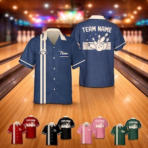 Pode incluir: Camisa de boliche azul marinho com detalhes brancos, gola creme e a palavra "Name" bordada no peito. A parte de trás da camisa apresenta "TEAM NAME" acima de um gráfico de pinos e bola de boliche. Camisas adicionais em vermelho, preto, rosa e verde.