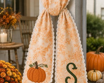 Peut inclure: Une décoration murale en tissu suspendue, en tissu orange clair avec un motif floral orange délicat et un bord festonné blanc. Un côté présente une citrouille orange brodée, tandis que l'autre côté arbore une grande lettre S vert foncé.