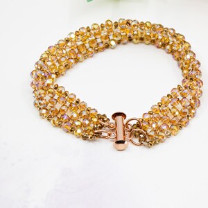 May include: A gold-toned bracelet with a multi-strand design featuring iridescent amber-colored beads. The bracelet has a lobster clasp closure.