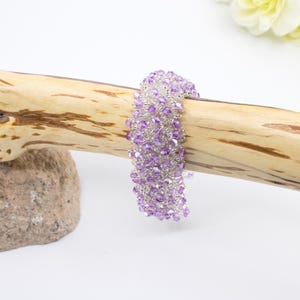May include: A purple and clear crystal beaded bracelet. The bracelet is made with small, faceted beads and is displayed on a wooden surface.