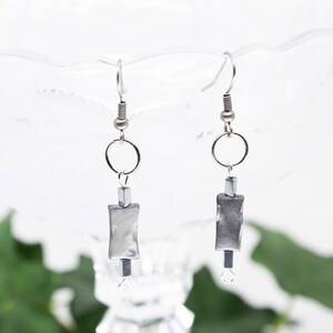 May include: A pair of silver dangle earrings with a rectangular silver bead and a small silver bead below it.