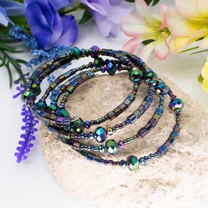 May include: A multi-strand bracelet made of iridescent blue, green, and purple beads. The bracelet is made of small square beads and larger round beads.