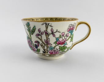 Puede incluir: Una taza de té de porcelana color crema con un diseño floral pintado a mano en tonos rosa, verde y azul. La taza cuenta con un borde y asa dorados, además de un patrón decorativo en la base y en el borde interior superior.