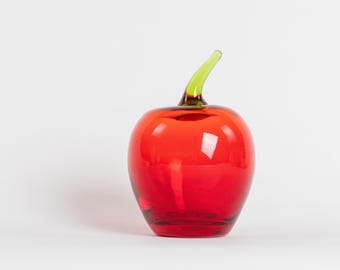May include: A decorative glass apple sculpture. The apple is a vibrant red color with a glossy finish. It has a green stem. The sculpture is set against a white background.