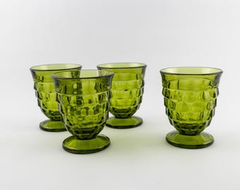 Puede incluir: Un juego de cuatro vasos de vidrio verde oliva con un patrón geométrico facetado y texturizado en el exterior. Cada vaso tiene una base circular ancha y un borde acampanado, fabricado en vidrio translúcido de color uniforme.