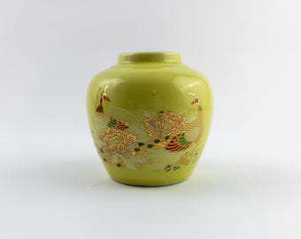 Puede incluir: Un jarrón de cerámica verde lima con cuerpo redondeado y cuello corto. La superficie presenta una detallada ilustración en tono dorado de dos pavos reales rodeados de grandes flores con toques de pintura esmaltada roja, verde y blanca.