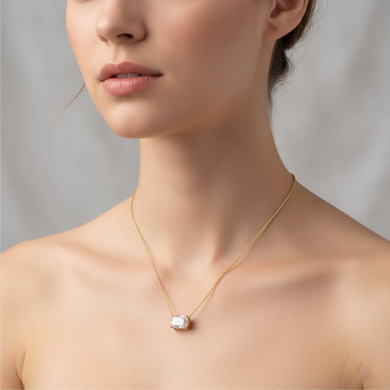 K&ouml;nnte beinhalten: Eine goldene Halskette mit einem rechteckigen, klaren Edelsteinanh&auml;nger. Der Anh&auml;nger ist in einer goldenen L&uuml;nette gefasst und h&auml;ngt an einer feinen Goldkette. Die Halskette wird vor einem neutralen Hintergrund pr&auml;sentiert.