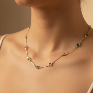 Peut inclure: Un collier en or délicat orné d'une série de pierres précieuses colorées. Le collier est composé d'une fine chaîne et orné de pierres rondes multicolores, notamment des gemmes bleues, vertes et roses. Le collier est porté autour du cou.