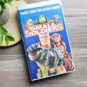 May include: A VHS tape for the film "Small Soldiers" with a blue cover featuring cartoon characters. The cover includes the text "SMART, FUNNY AND ACTION-PACKED!" and the film title in large, bold letters.
