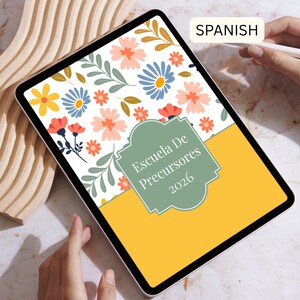 May include: A digital tablet displays a floral design with pink, blue, and yellow flowers, green leaves, and the text "Escuela De Precursores 2026" on a green label. The bottom of the screen is yellow.