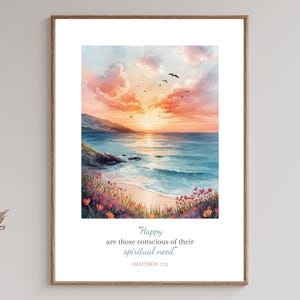 May include: A framed watercolor print depicts a coastal sunset scene. The artwork features a vibrant sky with orange and pink hues, a calm blue ocean, and a sandy beach with colorful flowers. The print includes the text "Happy are those conscious of their spiritual need".