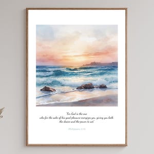 May include: Watercolor print of a beach scene with a sunset. The artwork features a vibrant sky with shades of orange, pink, and blue, reflecting on the ocean waves. The framed print includes a Bible verse at the bottom.