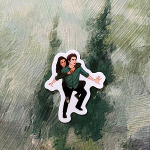 Puede incluir: Una pegatina que representa a una pareja abrazándose, con el hombre llevando a la mujer a la espalda. El hombre viste una camisa verde y pantalones negros, mientras que la mujer lleva una camisa verde oscuro. La pegatina tiene un borde blanco, sobre un fondo verde y blanco.