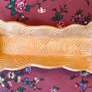 Peut inclure: Un plat en céramique orange en forme d'os, avec un motif texturé en forme d'éventail. Le plat est de couleur orange clair et a une finition brillante. Le plat est probablement utilisé pour servir ou exposer, environ 25 cm de long.