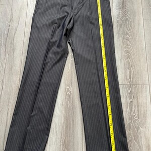 May include: Dark gray trousers with a subtle vertical pinstripe pattern, featuring a button closure at the waistband and a yellow measuring tape placed along the right leg, showing a length of approximately 42 inches from waist to hem.