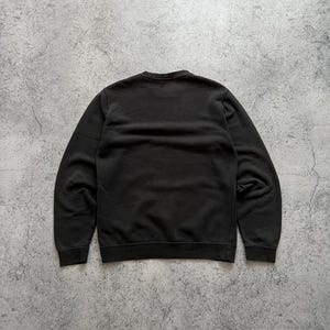 May include: A black crew neck sweatshirt. The sweatshirt is made of a soft material and has a ribbed neckline, cuffs, and hem. The back of the sweatshirt is visible in the image.
