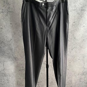 May include: Dark gray trousers featuring a subtle vertical pinstripe pattern, a button closure at the waistband, and side pockets. The trousers are displayed on a black M&S branded hanger, showcasing a straight-leg cut and a tailored appearance.