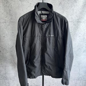 May include: Black Billabong jacket with a full-length zipper and a stand-up collar. The jacket has the Billabong logo on the chest and collar. The jacket is hanging on a black hanger.