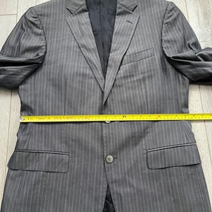 May include: A grey pinstriped blazer with a black interior lining, featuring two front buttons and two flap pockets. A yellow measuring tape is placed across the midsection, indicating a width of approximately 22 inches across the chest.