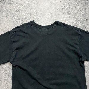 May include: A black crew neck t-shirt. The shirt is made of a soft material and has short sleeves. The t-shirt is plain and has no visible graphics or text. The shirt is slightly wrinkled.