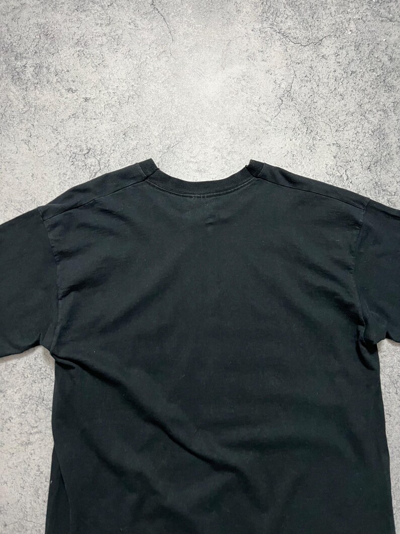 May include: A black crew neck t-shirt. The shirt is made of a soft material and has short sleeves. The t-shirt is plain and has no visible graphics or text. The shirt is slightly wrinkled.