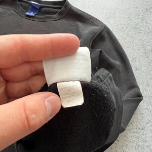 May include: Dark gray sweatshirt with a crew neck and a small blue tag. A white tag with black text and a Nike logo is visible. The sweatshirt is a size small.