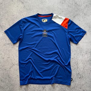 May include: A blue short-sleeved t-shirt with white and orange shoulder accents. The shirt features the text "EQUIPE DE FRANCE" and a gold logo. The shirt is a size XL.