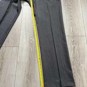 May include: Dark gray trousers with a subtle vertical pinstripe pattern. A yellow measuring tape is placed along the inner seam, showing a length measurement extending from the crotch to the hem, reaching approximately 32 inches in total.
